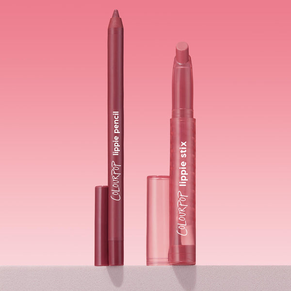 ColourPop Lippie Pencil Shot Clock stands uncapped beside matching Lippie Stix, both in rosy mauve, upright on a light surface against a pink gradient backdrop, highlighting the precise liner tip and branded tubes.