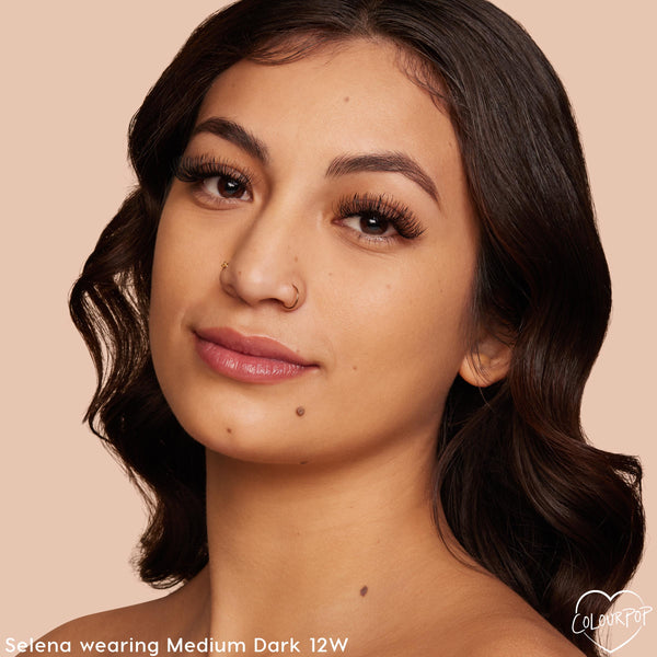 Model wearing ColourPop Pretty Fresh Tinted Moisturizer in Medium 12 W, showcasing a dewy, natural finish with light coverage on warm-toned skin; close-up portrait against a soft beige studio background.