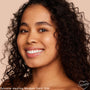 Model smiling in a close-up, wearing ColourPop Pretty Fresh Tinted Moisturizer in Medium Dark 15 W, showing dewy, even coverage and natural finish against a soft beige background.