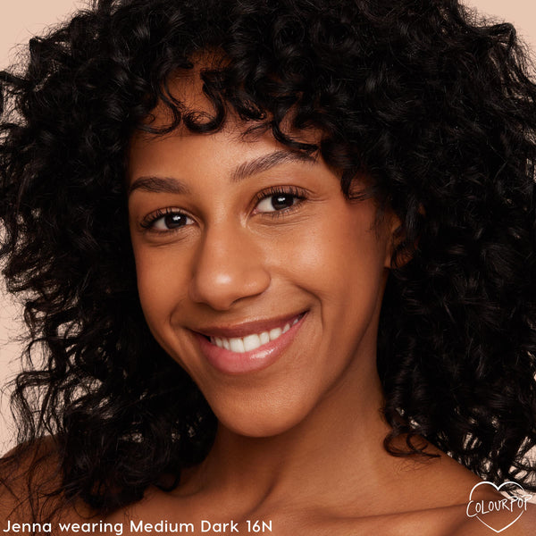Model wearing Medium Dark 16 N shade, showing even, natural coverage and a soft glow from the ColourPop Pretty Fresh Tinted Moisturizer in a close-up smile against a peach studio background, highlighting the neutral undertone.