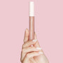 ColourPop Ultra Glossy Lip in Major Throwback held upright by a manicured hand, showcasing a neutral nude-pink gloss in a clear tube with a white cap against a soft pink background.