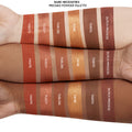 Swatches show the Bare Necessities ColourPop Shadow Palette pressed powders, Haute, Fuzzy, Tabloid, Genie, Taboo, Dutch Process, applied in stripes on three arms of different skin tones to compare pigment and finish.