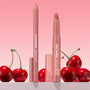 ColourPop Lippie Pencil "Oh Snap" stands uncapped with a creamy soft pink-nude tip, paired with matching Lippie Stix, on a countertop with glossy red cherries against a pink gradient backdrop - ideal for precise, long-wear lip lining.