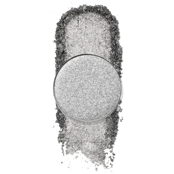 On a Whimsy pressed powder shadow by ColourPop, a cool-toned metallic silver single pan, catching light as the shade is swatched in a dense shimmer trail with loose glittery pigment on a white background.