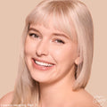 Model wearing ColourPop Pretty Fresh Tinted Foundation Balm, shade Fair 3, smiling in a close-up; skin appears even, dewy, and natural with lightweight, buildable coverage against a warm beige background.