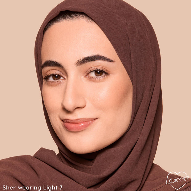 Model wearing ColourPop Pretty Fresh Tinted Foundation Balm in Light 7, showcasing smooth, natural dewy coverage; close-up face in a brown headscarf against a beige background to display the true shade and finish.