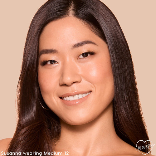 Model wearing ColourPop Pretty Fresh Tinted Foundation Balm in Medium 12, showcasing dewy, natural coverage and an even complexion in a close-up portrait against a warm beige background.
