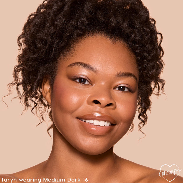 Model smiles wearing ColourPop Pretty Fresh Tinted Foundation Balm in Medium Dark 16, showing smooth, dewy, medium coverage in a close-up studio shot against a beige background with soft blush and glossy lips.
