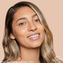 Model smiling wears ColourPop Pretty Fresh Creamy Concealer, shade Medium Dark 115 W (warm), showcasing smooth medium-dark coverage and a dewy finish on even-toned skin against a soft beige background.