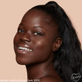 Smiling model showcases ColourPop Pretty Fresh Creamy Concealer in Deep Dark 220 C, revealing smooth, radiant, skin-like coverage; close-up studio portrait with glossy lips, high ponytail, and peach background with ColourPop logo.