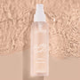 ColourPop Pretty Fresh Setting Spray, Lock It In, stands upright with a white pump on a frosted blush bottle labeled peptides + niacinamide, casting a soft shadow against rippled beige water for a clean, dewy makeup-locking look.