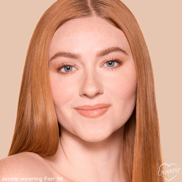 Model wearing Fair 1 N, a light neutral shade of ColourPop Pretty Fresh Tinted Moisturizer, showcasing natural dewy coverage with soft peach gloss and subtle lashes against a beige backdrop, emphasizing smooth, even skin and a radiant finish.