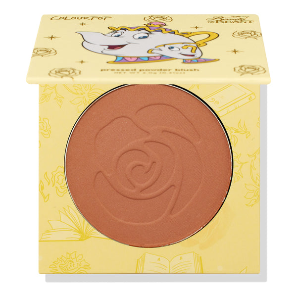 Chip ColourPop Pressed Powder Blush compact - half-open to show a warm rosy terracotta pan embossed with a rose - rests in yellow Disney Beauty and the Beast packaging featuring Mrs. Potts and Chip illustrations and gold rose motifs.