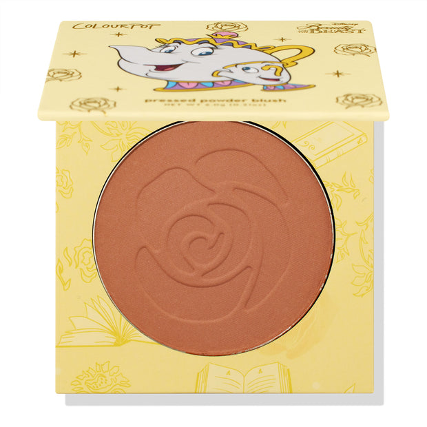 Chip ColourPop Pressed Powder Blush compact - half-open to show a warm rosy terracotta pan embossed with a rose - rests in yellow Disney Beauty and the Beast packaging featuring Mrs. Potts and Chip illustrations and gold rose motifs.