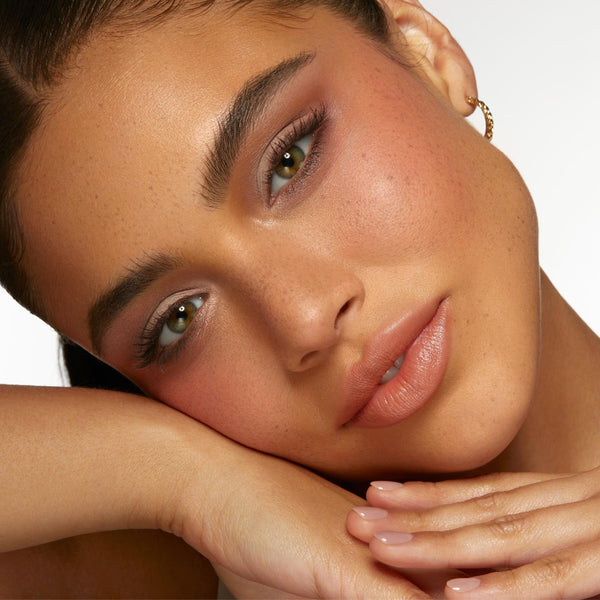 Neutral eye makeup showcasing Going Coconuts ColourPop Shadow Palette - soft taupe and cocoa shimmers on lids with defined lashes - model resting face on hands under studio light against a white backdrop, paired with peachy blush and nude gloss.