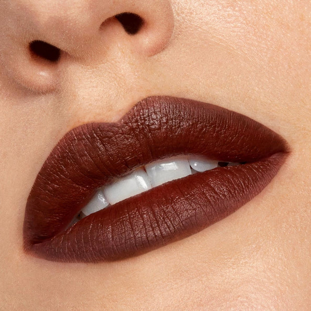 Full lips lined and filled with Pitch, a deep chocolate-brown ColourPop Lippie Pencil, delivering velvety matte coverage and crisp edges as the mouth slightly parts to reveal white teeth in a close-up beauty shot.