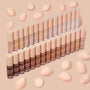 ColourPop Pretty Fresh Creamy Concealer, shade Light 50 W, standing with the full shade range in neat rows; frosted tubes with blush-pink caps and peach blending sponges scattered on a nude background.