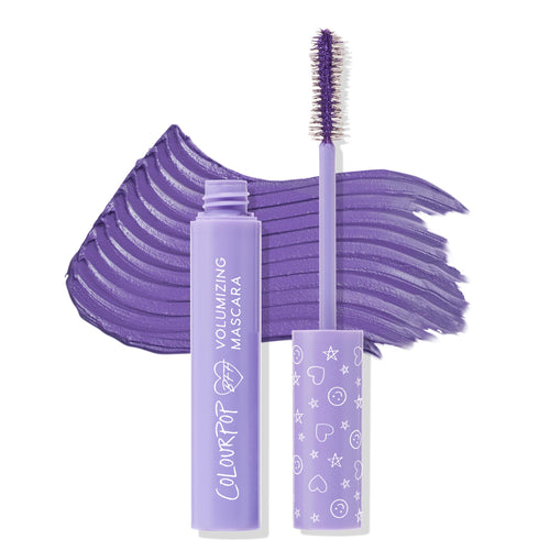 Purple Prose ColourPop BFF Mascara shown open, wand coated in rich violet sweeping across a bold swatch, beside a lavender volumizing tube and a cap with hearts, stars, and smiley icons on a white background.