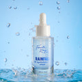 Fourth Ray Beauty Rainfall 2% HA Serum dropper bottle standing upright, catching water splashes against a light-blue backdrop, showcasing its hydrating hyaluronic acid formula; ColourPop Face Serum, 0.95 fl oz/28 mL.