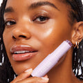 A-LIST BABE youth-boosting serum stick in a lavender tube pressed to a model’s cheek, creating a dewy highlight beside glossy lips, showcased as part of the Best Face Scenario ColourPop Face Set for radiant, hydrated skin.