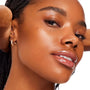 Model’s close-up face showcases a dewy, pore-smooth glow with glossy lips and natural brows, demonstrating the So Refined ColourPop Face Set on a studio white background, with a small gold geometric hoop earring visible.