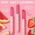 Delulu So Juicy Plumping Gloss Balm with Peptides by Colourpop shown as three pink lip balm sticks standing upright on a pink background, surrounded by grapefruit and strawberry slices, highlighting hydrating Lip Gloss & Lip Oil ingredients like hyaluronic acid, ceramides, peptides, and ginger for visibly plump lips.
