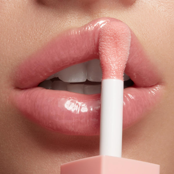 Doe-foot applicator applies Baby Panda shade of ColourPop So Juicy Plumping Glossy Lip Oil to smooth, full lips, delivering a high-shine, plumped, soft pink finish in a close-up studio beauty shot.