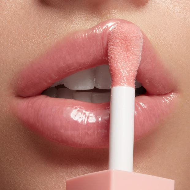 Doe-foot applicator applies Baby Panda shade of ColourPop So Juicy Plumping Glossy Lip Oil to smooth, full lips, delivering a high-shine, plumped, soft pink finish in a close-up studio beauty shot.