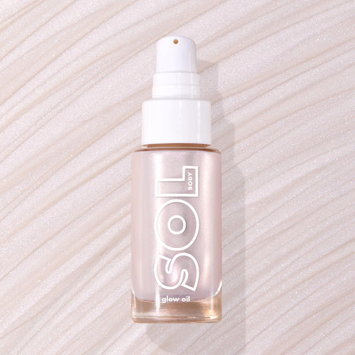 Moonstone SOL Body glow oil bottle displaying pearly pink luminizer through frosted glass with white pump, resting flat on a swirled, shimmery nude backdrop; ColourPop SOL Glow Oil for a radiant body glow.