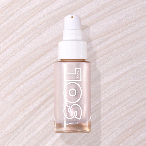 Moonstone SOL Body glow oil bottle displaying pearly pink luminizer through frosted glass with white pump, resting flat on a swirled, shimmery nude backdrop; ColourPop SOL Glow Oil for a radiant body glow.