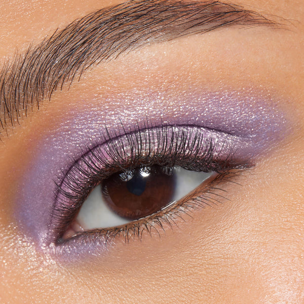 Shimmering lavender-pink eyelid wearing Rose Garden, a ColourPop Super Shock Shadow, blended across lid and lower lash line with metallic sheen and fine sparkle, accenting a brown eye and soft lashes in a tight close-up beauty shot.