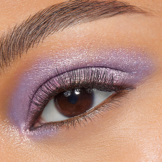 Shimmering lavender-pink eyelid wearing Rose Garden, a ColourPop Super Shock Shadow, blended across lid and lower lash line with metallic sheen and fine sparkle, accenting a brown eye and soft lashes in a tight close-up beauty shot.