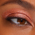 Shimmering copper eyeshadow coats a brown eye, showcasing Flamethrower, a metallic shade of ColourPop Super Shock Shadow, with glittery payoff swept across the lid and crease, accenting soft lashes and skin texture in a tight beauty close-up.