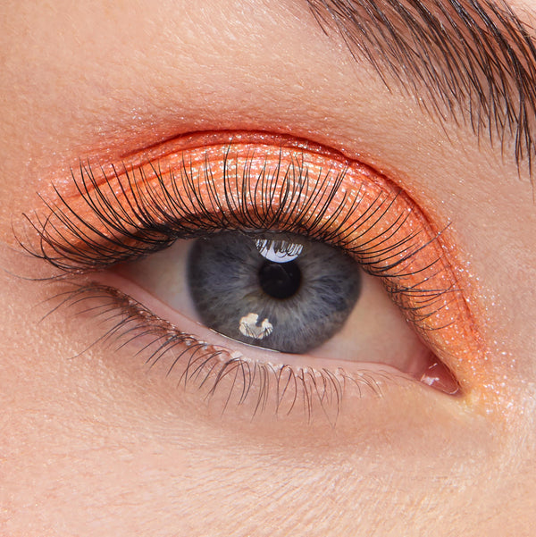 Shimmery metallic orange eyeshadow with fine gold sparkle sweeps across the upper lid, showcasing ColourPop Super Shock Shadow Flamethrower on a close-up eye with long lashes for a fiery, high-shine finish.