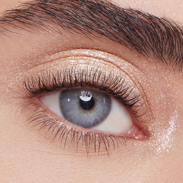 Ladybird Super Shock Shadow by ColourPop shimmering on eyelid - sparkly champagne-beige glitter eyeshadow swept across lid and inner corner for a metallic glow - shown in a close-up eye with long lashes and a defined brow.