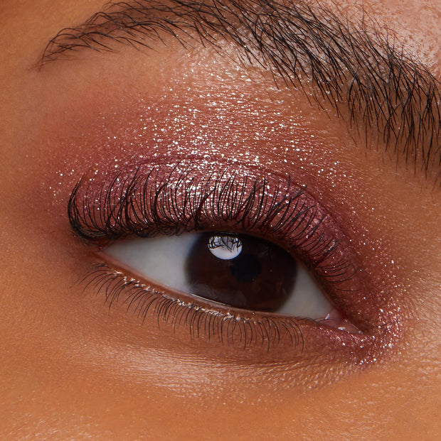 Shimmery rose‑plum shadow catching light across a model’s eyelid and inner corner, with defined lashes, showcasing ColourPop Party of Five Super Shock Shadow’s sparkly, metallic finish in a tight beauty close-up.