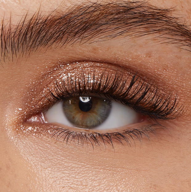 Shimmering eyelid showcases ColourPop Super Shock Shadow Ritz, a sparkly champagne‑taupe eyeshadow swept across the lid and inner corner, catching light beside full lashes in a tight close-up beauty shot.