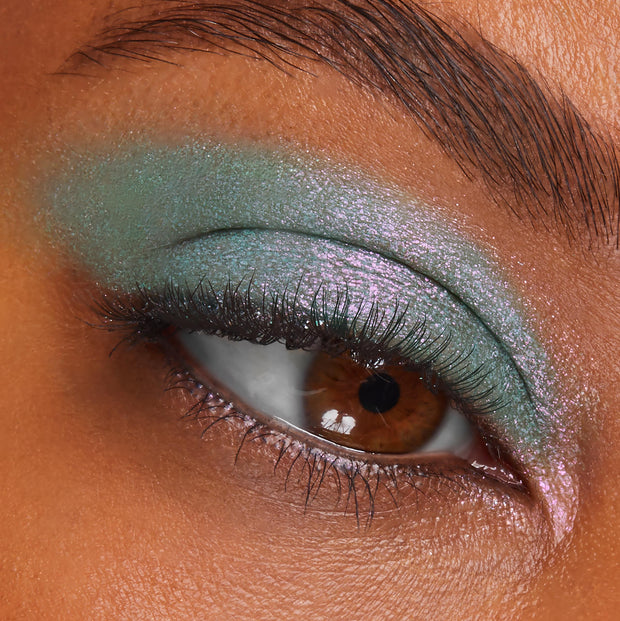 Shimmery teal-to-pink duochrome eyeshadow sweeps across an eyelid with defined lashes; ColourPop Super Shock Shadow Solar Beam showcases high-shine metallic payoff and inner-corner highlight in a close-up.
