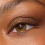 ColourPop Super Shock Shadow in We Won't Bite coats the upper eyelid with metallic olive-bronze shimmer, softly blended into the crease with fine gold sparkle, shown in a macro close-up highlighting texture and color payoff.