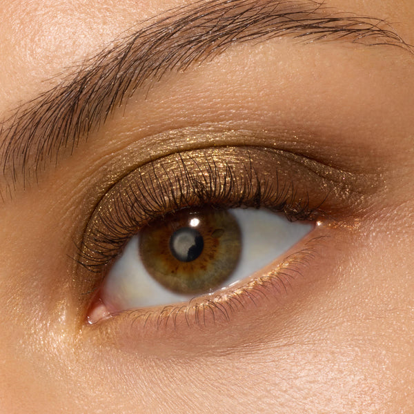 Shimmering antique-gold eyeshadow coats a single eyelid, blended into a warm bronze haze at the outer corner, showcasing ColourPop Super Shock Shadow We Won't Bite with a smooth metallic, cream-to-powder finish in a macro beauty swatch.