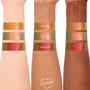 ColourPop Shadow Stix Love Triangle arm swatches shown on light, medium, and deep skin: Wolf Girl duochrome gold-green, It’s Always Been Him peach shimmer, and Vampire Girl red-gold, photographed against a clean white backdrop.
