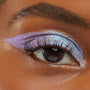 Close-up of an eye wearing Colourpop Disco Disco Shadow Stix, showcasing metallic lavender and icy blue shimmer layered across the lid and winged outwards against smooth medium-brown skin, highlighting bold, multidimensional eye makeup.