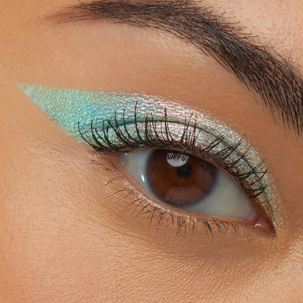 Close-up of a brown eye wearing Colourpop Game Over Shadow Stix, showcasing a sharp, winged swipe of shimmery mint-green and pink duochrome eyeshadow across the upper lid for a bold, metallic finish.