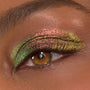 Close-up eyelid showcasing It's Always Been Him Shadow Stix, a ColourPop Shadow Stix shade, with multichrome pink, green, and gold metallic shimmer sweeping across the lid and crease on a brown eye, smoothly blended with fine sparkle.