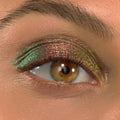Shimmering eyelid wears Love Triangle ColourPop Shadow Stix, shifting pink‑green‑gold across the lid in a metallic multichrome finish; extreme close-up of one eye with natural lashes and brow showing color payoff.