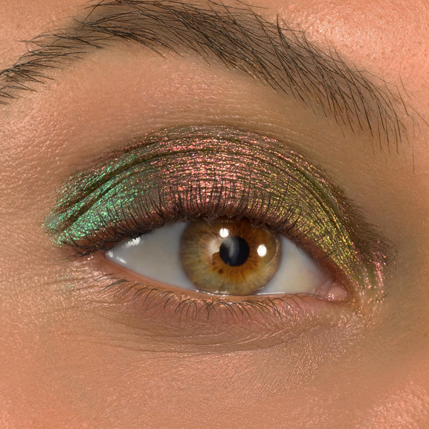 Shimmering eyelid wears Love Triangle ColourPop Shadow Stix, shifting pink‑green‑gold across the lid in a metallic multichrome finish; extreme close-up of one eye with natural lashes and brow showing color payoff.