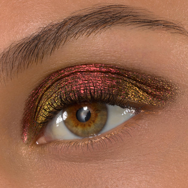 Vampire Girl ColourPop Shadow Stix sweeps across a hazel eye, creating a metallic multichrome look that shifts from ruby red to antique gold on the upper lid, framed by defined lashes and a natural brow in a macro beauty shot.