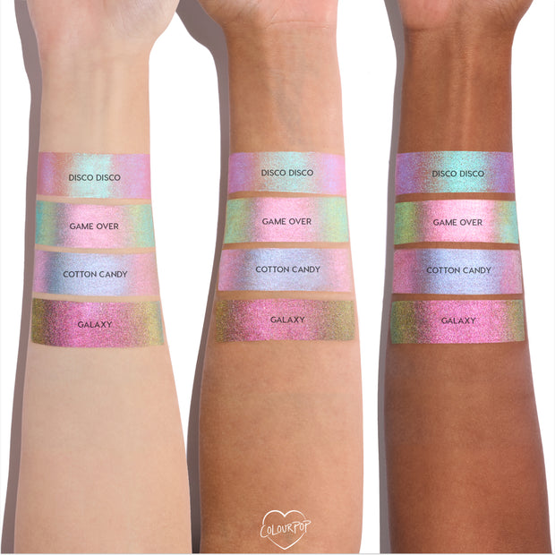 Colourpop Shadow Stix Galaxy shade swatched on three different skin tones, showing a wide band of metallic pink-to-gold multichrome shimmer beneath other pastel shades for comparison on bare forearms.
