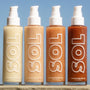 ColourPop SOL Shimmering Dry Oil in Warm Gold stands beside three deeper bronze shades, pumps up, sparkling in sunlight on a stone ledge against a blue sky; tall 3 fl oz bottles with bold SOL logo show golden shimmer.