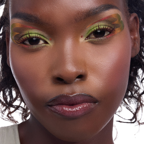 Model wearing Shrek-inspired eye look - lime and olive shadows with wavy brown edges and tiny red inner-corner dots - plus glossy plum lips - in a studio close-up, highlighting the ColourPop X DreamWorks Shrek Full Collection Set, a ColourPop Full Collection Set.